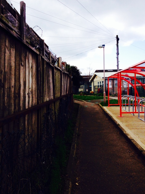 photo of path past rickety fences and red bike shelter